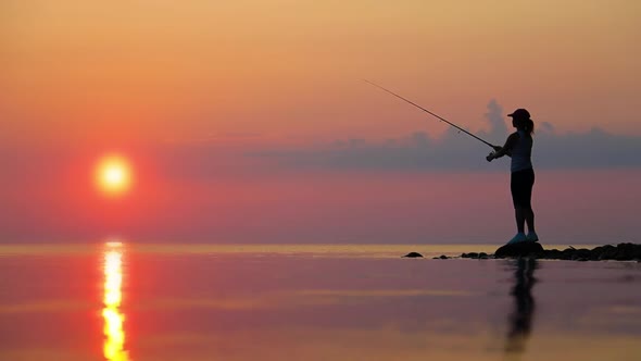 Woman Fishing on Fishing Rod Spinning at Sunset Background