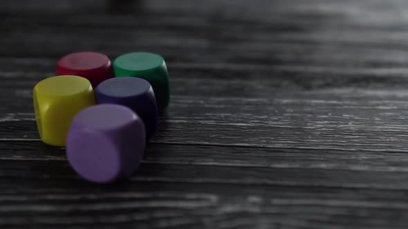 5 game colored dice glide over the dark wooden old table and stop to the left. 