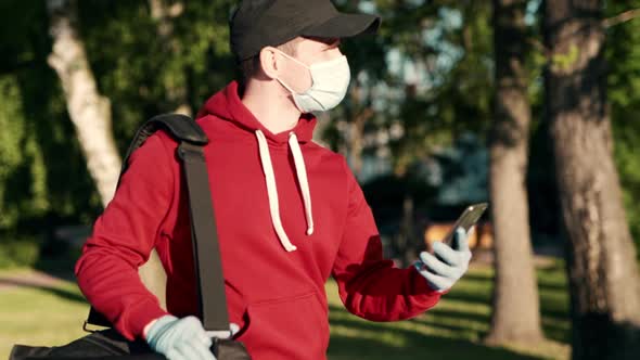 Asian Delivery Man in Red Uniform with Face Mask Carrying Bag of Food Delivering Food to Customer