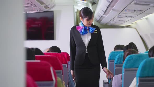 Asian beautiful female flight attendant or air hostess walking on aisle checking and giving service.