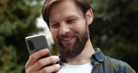 Portrait of Cute Caucasian Young Man is walking in Park, Texting Messages.