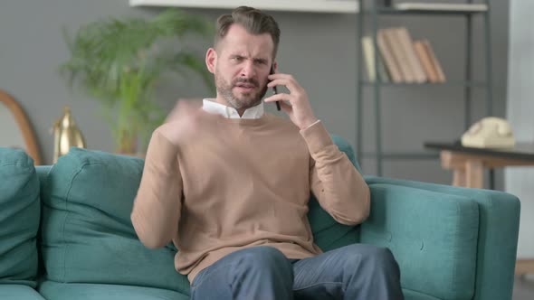 Angry Man Talking on Smartphone on Sofa