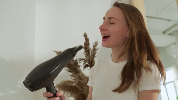 Happy Woman with Hair Dryer Sings at Home