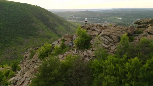 Aerial reveal forward of young man hiking on a rocky cliff in Pennsylvania showing the forest and ri