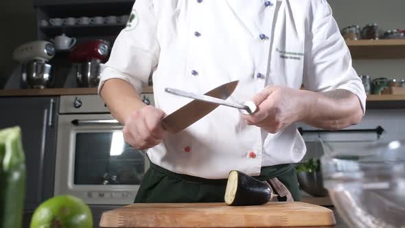 chef in modern kitchen of restaurant sharpens a knife for cutting vegetables.