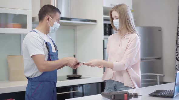 Service Man Receiving Payment From Positive Young Caucasian Woman in Covid19 Face Mask