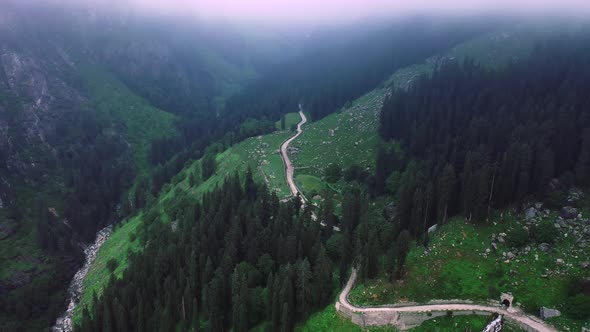 Aerial Shot of a Road Diverging Into the Mountains During Monsoon Framed By Clouds in Manali