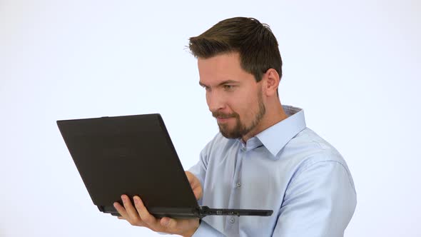 A Young Handsome Man Looks Mischievously Around and Works on a Computer - White Screen Studio