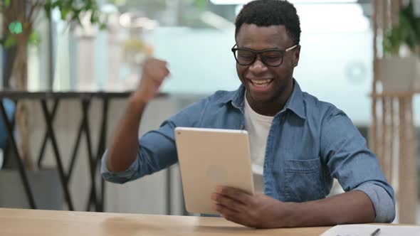 Successful Young African Man Celebrating on Tablet in Modern Office