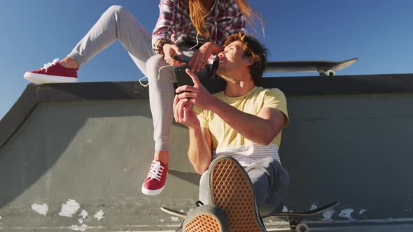 Happy caucasian female and male friends using smartphone on sunny day