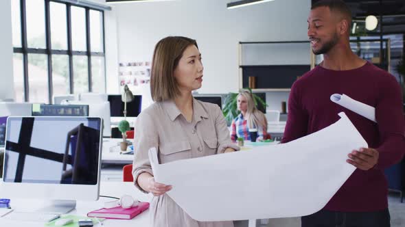 Diverse male and female office colleagues discussing over blueprint plan at modern office