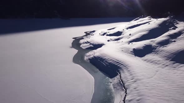 Aerial view over the shore of a melting frozen lake to a huge mountain panorama with big snowy mount