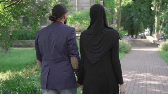 Back View of Romantic Muslim Couple Walking in Park and Talking. Camera Follows Loving Bearded Man