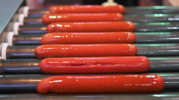 Rolling Juicy Sausages on the Hotdog Grill Closeup