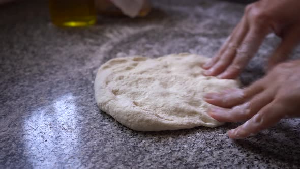 Chef kneading homemade pastry dough on flour work surface, closeup