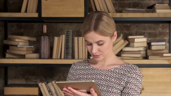 Pleasant woman using tablet on books background. Close up side view.