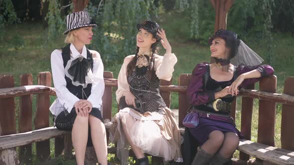 Wide Shot Three Happy Slim Beautiful Caucasian Women in Steampunk Costumes Sitting in Sunshine