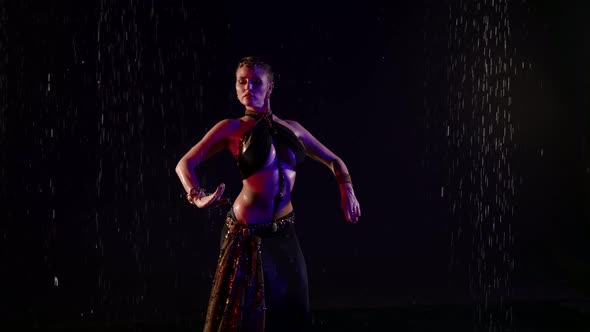 A Beautiful Woman is in the Pouring Rain in a Studio on a Black Background Dancing an Oriental Dance