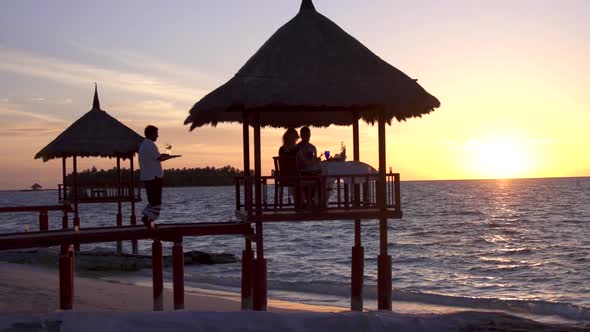 A man and woman couple eat dinner and dine in a hut on a tropical island beach