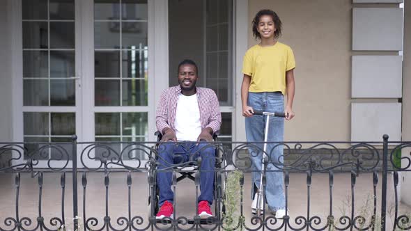 Portrait of Happy African American Disabled Father in Wheelchair and Teenage Daughter with Kick