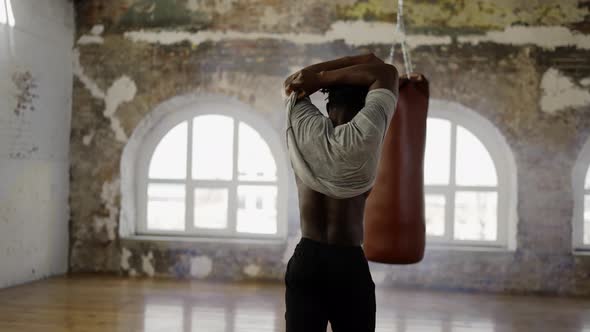 African American Athlete Walking Into Room with Boxing Pear Taking Off Shirt Rear View