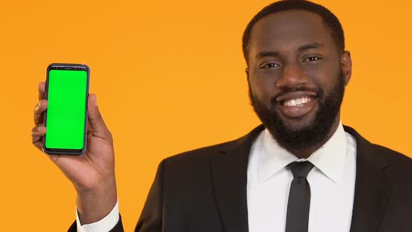 African-American Male in Suit Showing Smartphone With Green Screen and Winking
