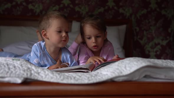 Two Cute Smiling Preshool Toddler Children on Pajamas Read Book of Fairy Tales on Bed