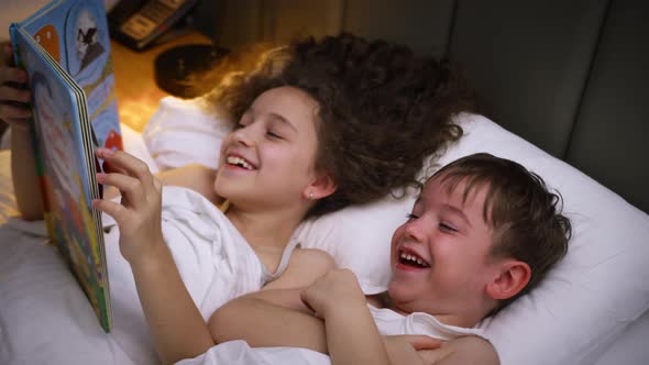 Child Care at Home Little Sister Takes Care of Younger Brother Reads a Bedtime Story to Children