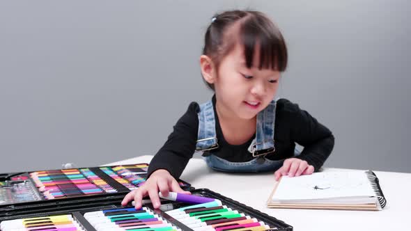 Little young Asian girl concentrate on choosing color magic pen for painting picture on notebook. Li