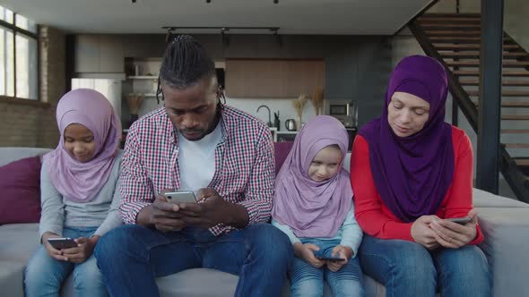Positive Diverse Multiracial Muslim Family with Little Girls Browsing Online on Smartphones Indoor