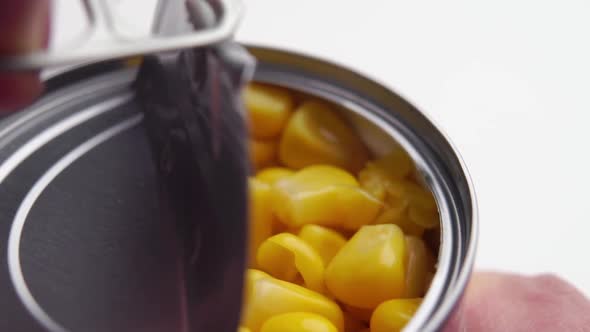 A finger pulling on the ring opens the aluminum lid of the canned corn can