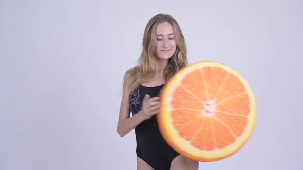 Happy Young Blonde Woman in Swimsuit Biting Orange Pillow As Healthy Concept
