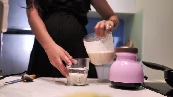 Close Up on a Woman Pouring Healthy Banana Smoothie Into a Glass in the Kitchen