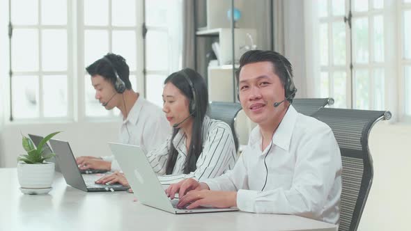 A Man Of Three Asian Call Centre Agents Smiling To Camera While His Colleagues Speaking To Customers