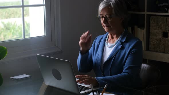 Senior woman sitting in office typing on laptop