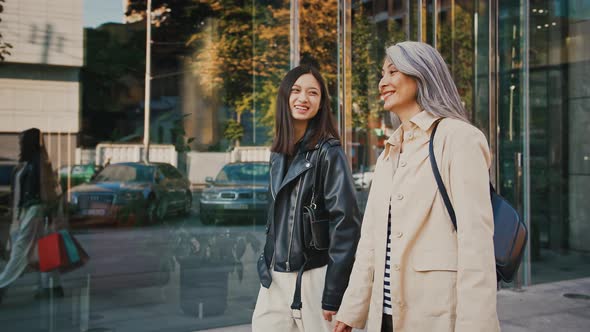 Asian Middleaged Mom and Adult Daughter Smiling Talking Carrying Shopping Bags Walking By Street