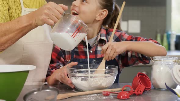 Girl mixing the flour while grandmother pouring milk into the bowl 4K 4k