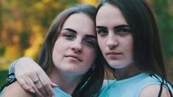 Twins Girls Embracing Look at the Camera in Green Nature Background. Slow Motion