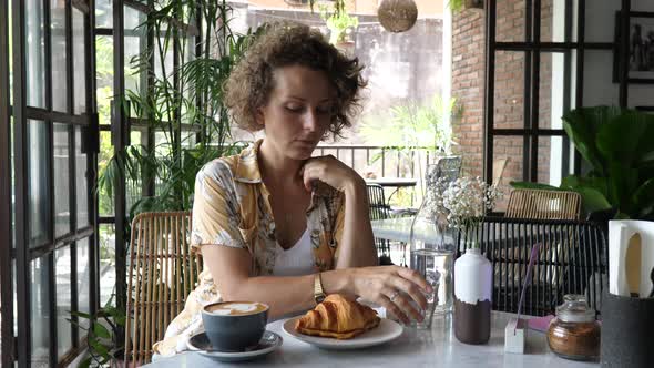 Caucasian Woman Takes Off Her Face Mask to Have a Coffee with Croissant in Stylish Cafe