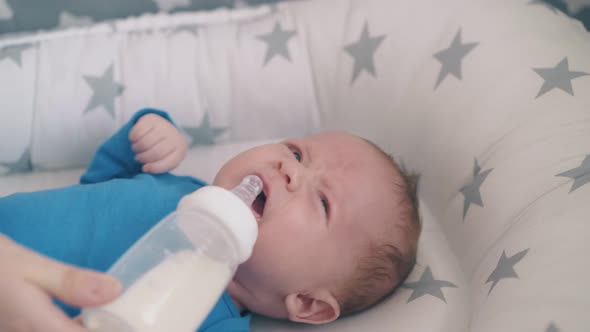 Mommy Gives Bottle with Milk to Crying Baby in Soft Cocoon