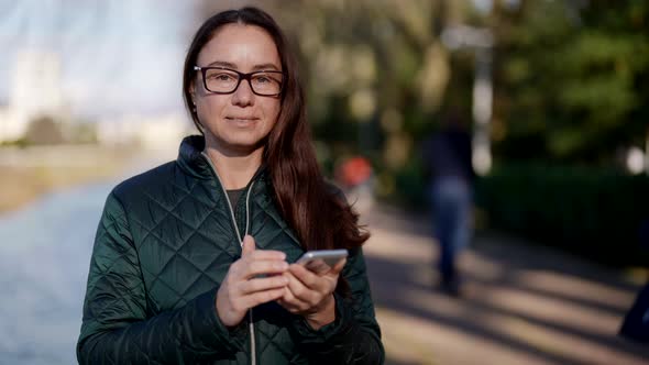 Calm Joyful Woman is Using Smartphone on City Street Smiling and Looking at Camera