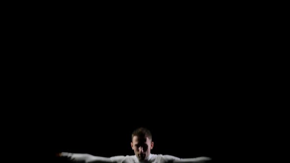 Young Handsome Male Acrobat Gymnast in White Clothes on a Black Background Jumping on a Bot-up