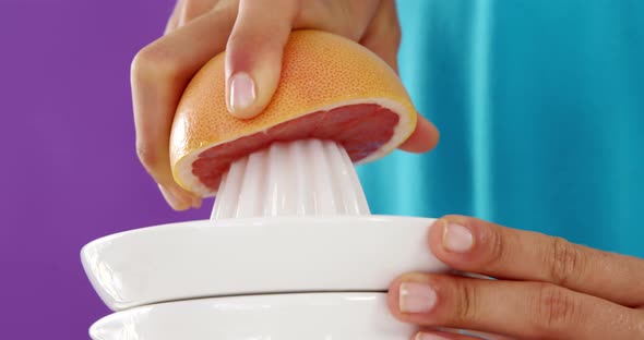 Woman preparing blood orange juice from juicer against violet background