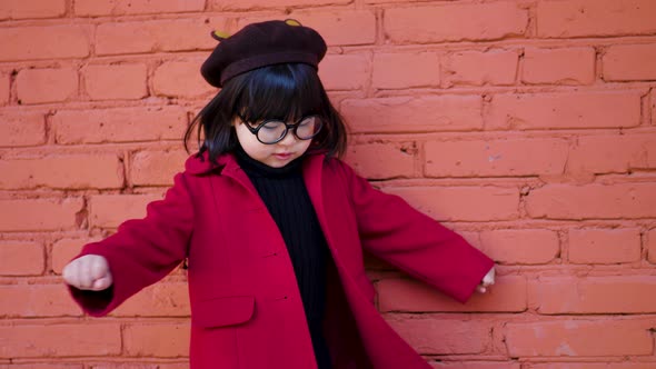 Korean Girl in a Red Coat and Cap and Round Glasses Dance on Red Brick Wall the Street in Autumn