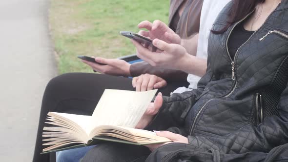 Friends Are Sitting on Bench in the Park in the Summer and Reading a Book