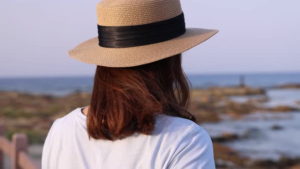 Young woman standing by the sea and wearing straw hat