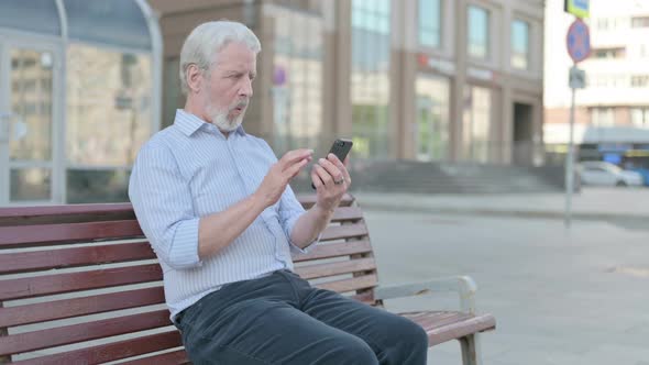 Old Man Reacting to Loss on Smartphone While Sitting Outdoor on Bench