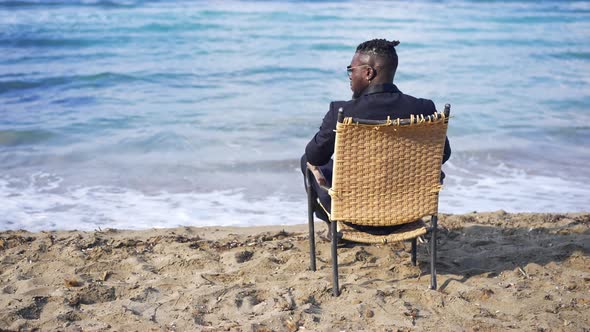 Back View Wicker Chair with African American Young Man in Formal Suit Sitting Admiring Beauty of