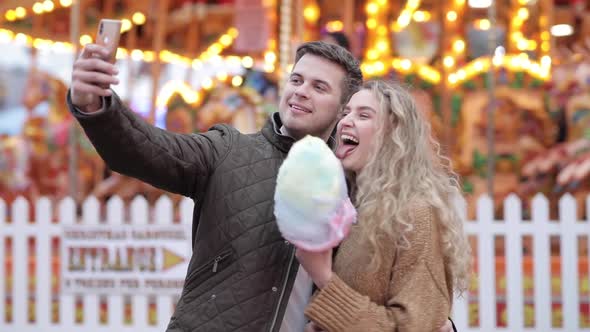 Happy couple taking a selfie at amusement park and eating cotton candy