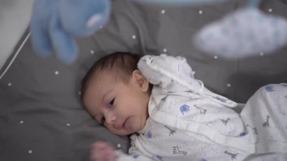 A Newborn Baby Lies in a Crib and Looks at a Toy Mobile